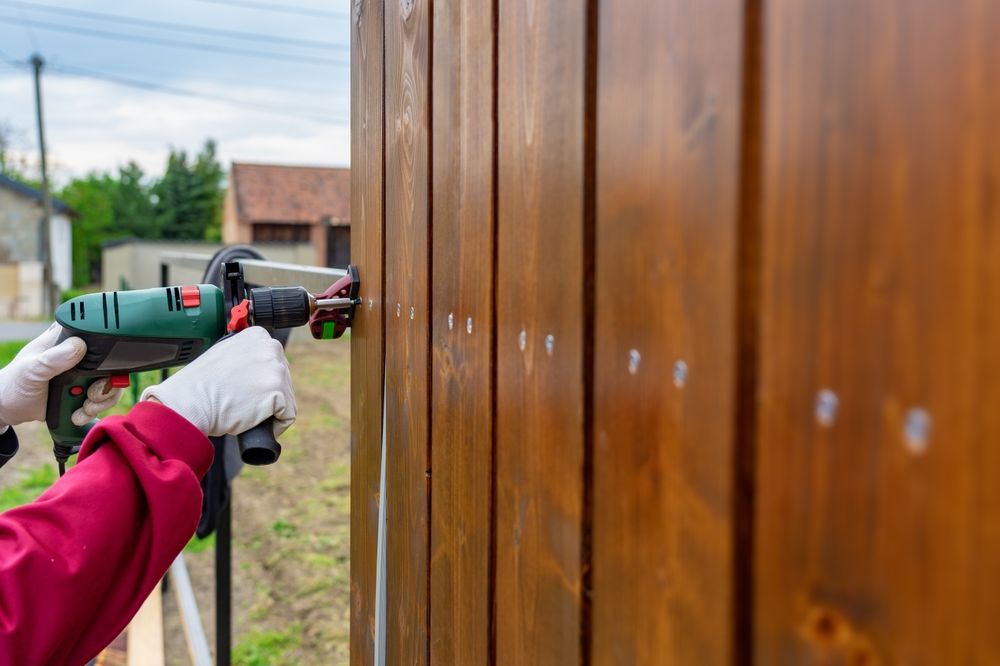 A man uses a power drill to help build a wood fence